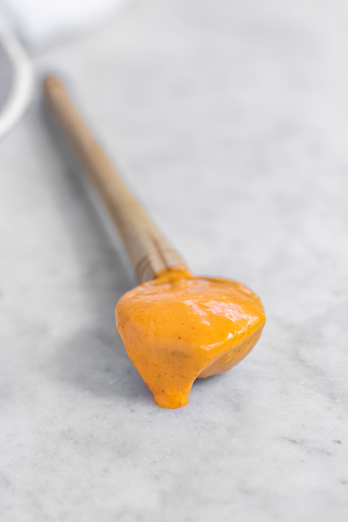 Orange gochujang aioli in a spoon on a white counter.