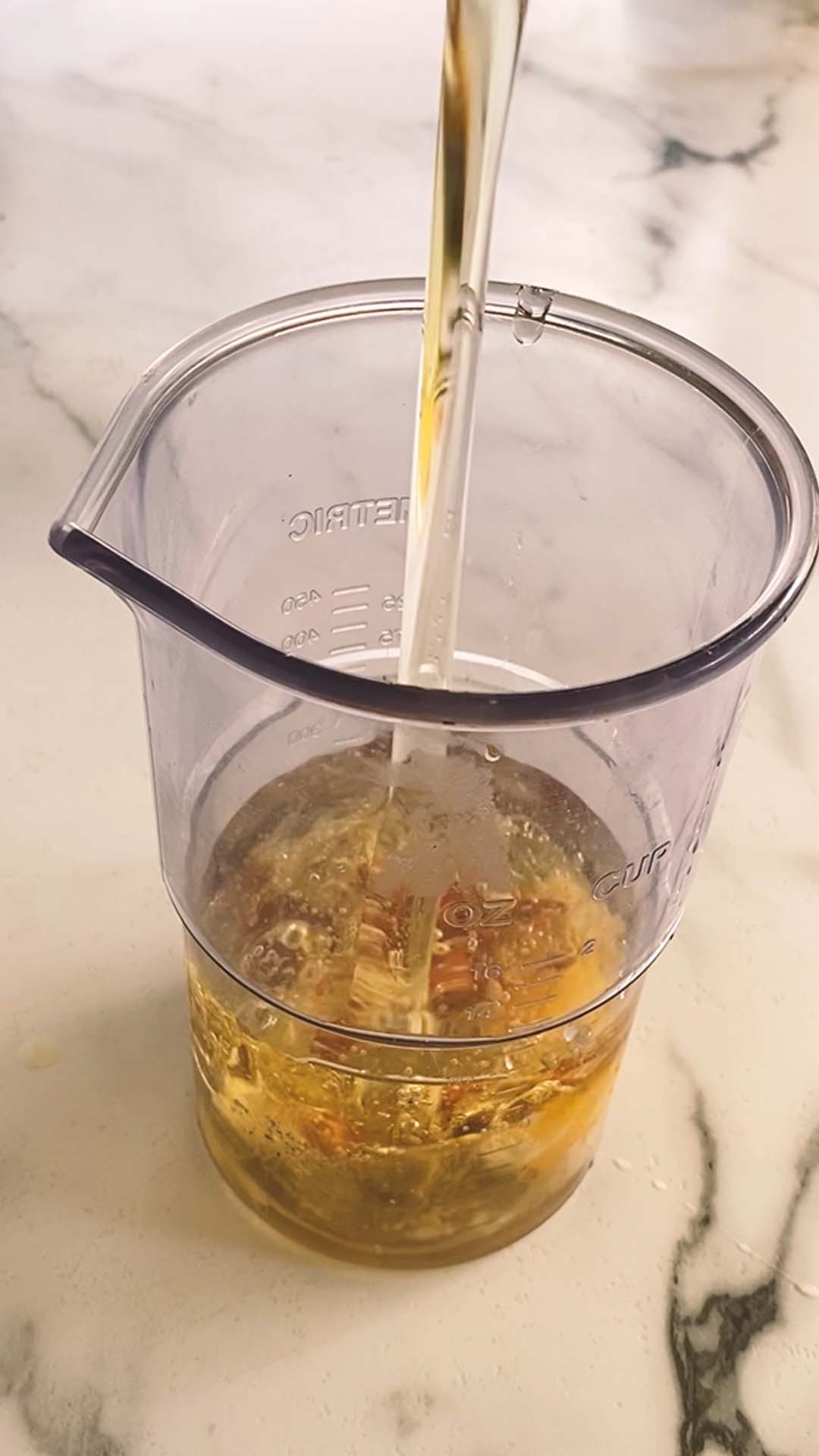 Pouring oil in to a tall container with other ingredients in it.