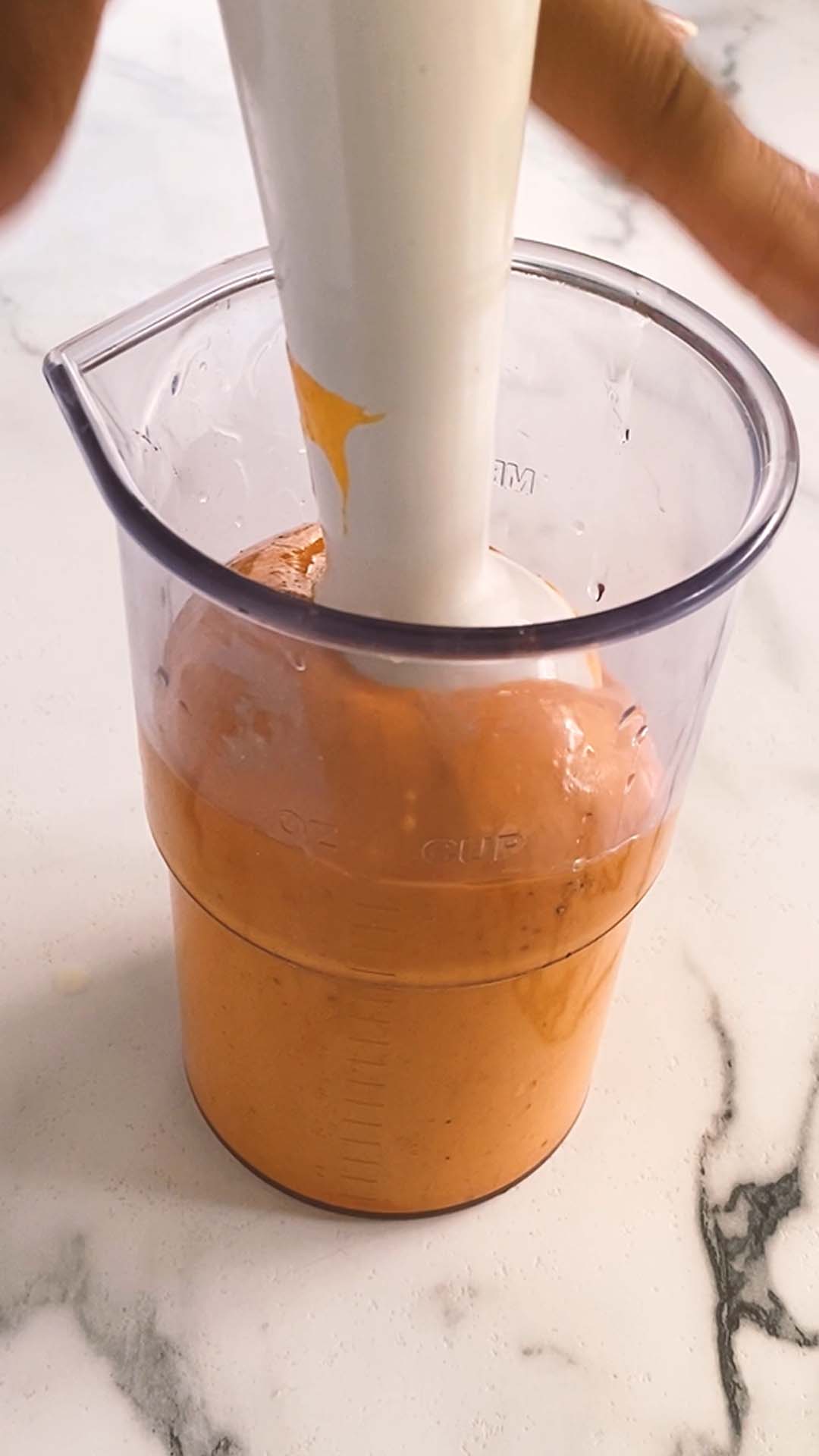Using an immersion blender to blend gochujang aioli in a tall container.
