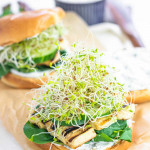 A burger bun stuffed with spinach, grilled halloumi, cucumbers, alfalfa sprouts, and a yogurt spread.,