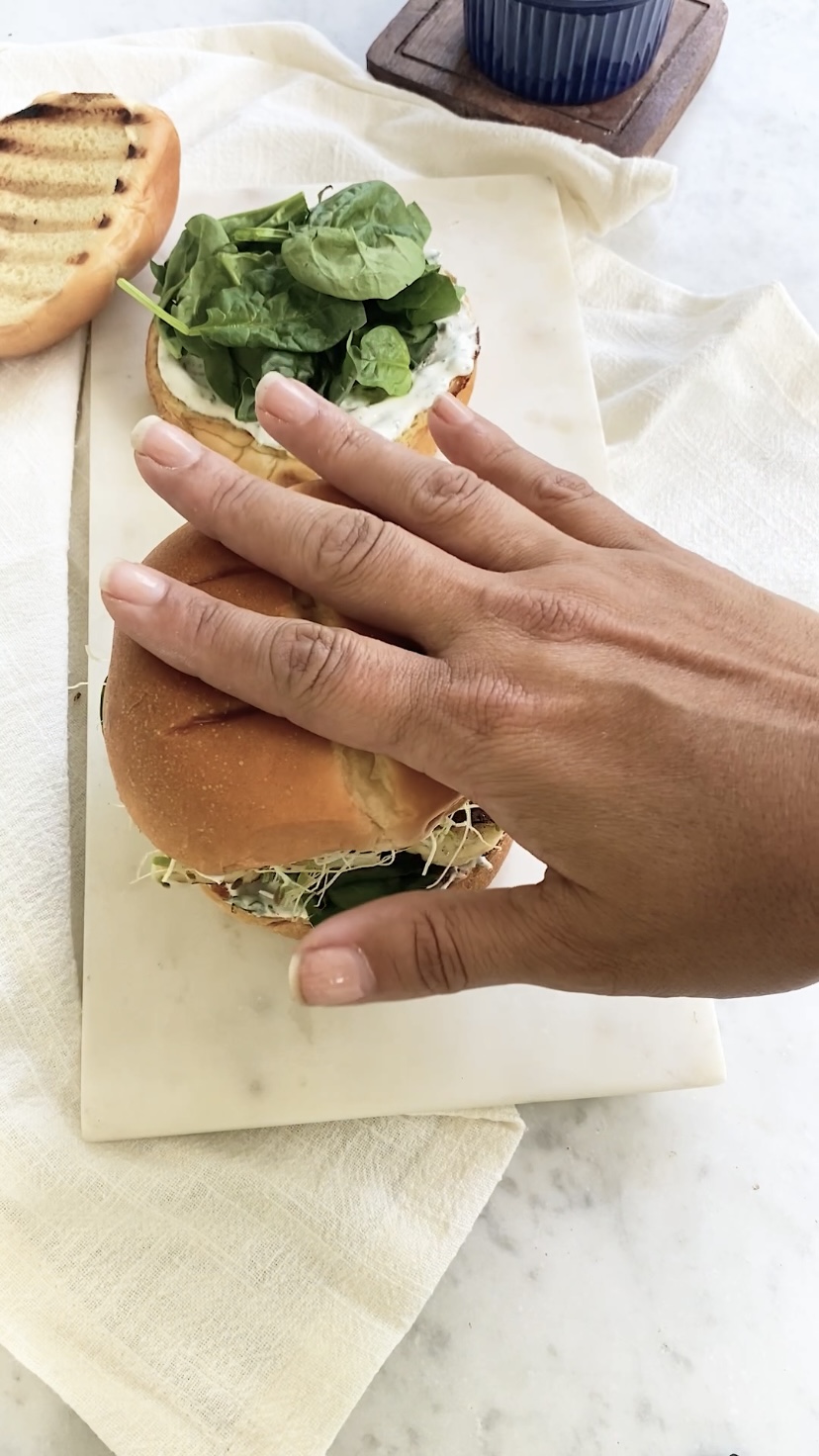 A hand adding the top bun to a burger.