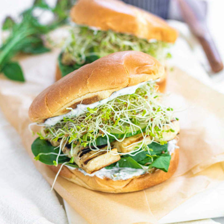 A burger bun stuffed with spinach, grilled halloumi, cucumbers, alfalfa sprouts, and a yogurt spread.,