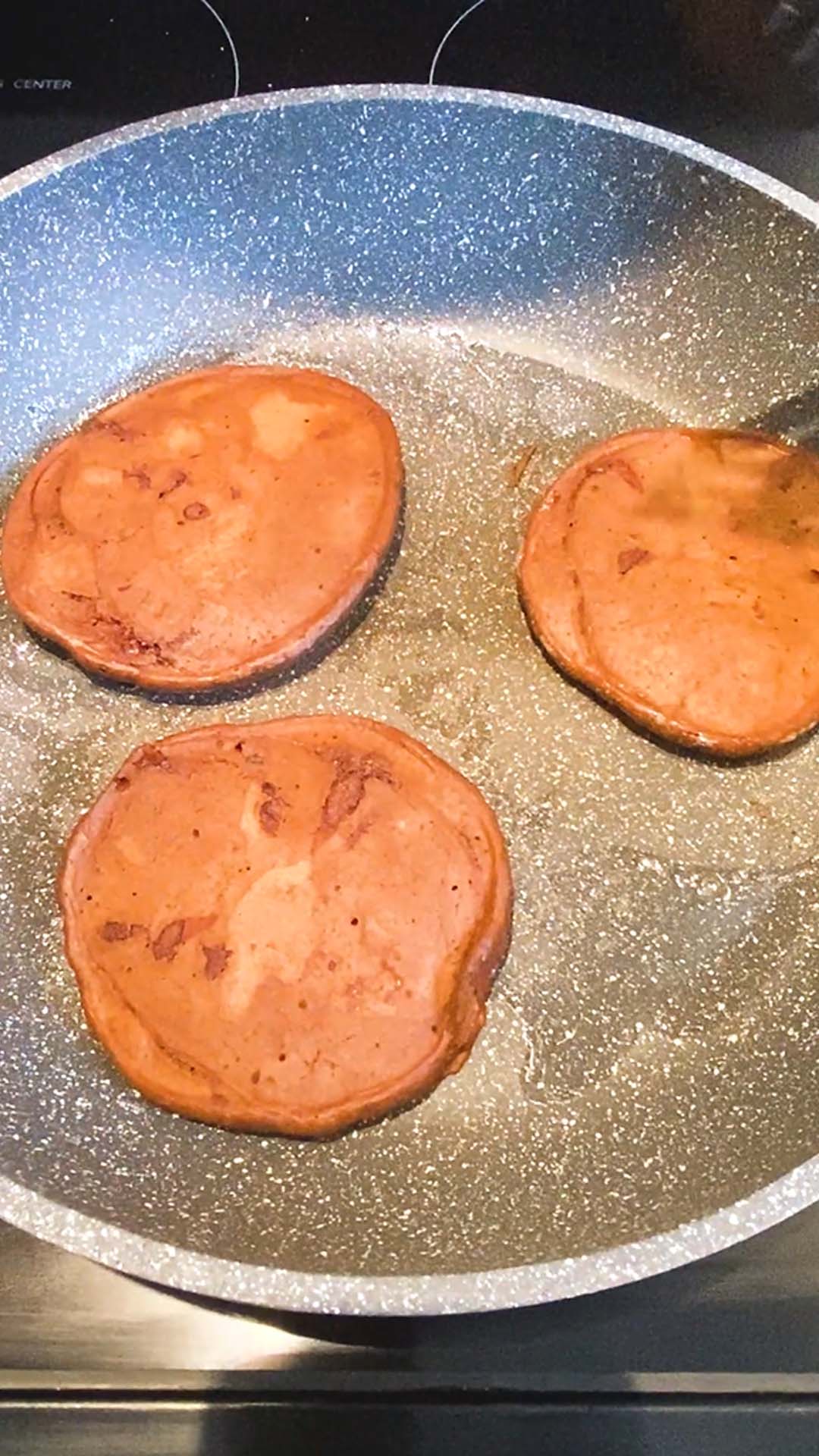 Three pancakes being cooked after having been flipped.