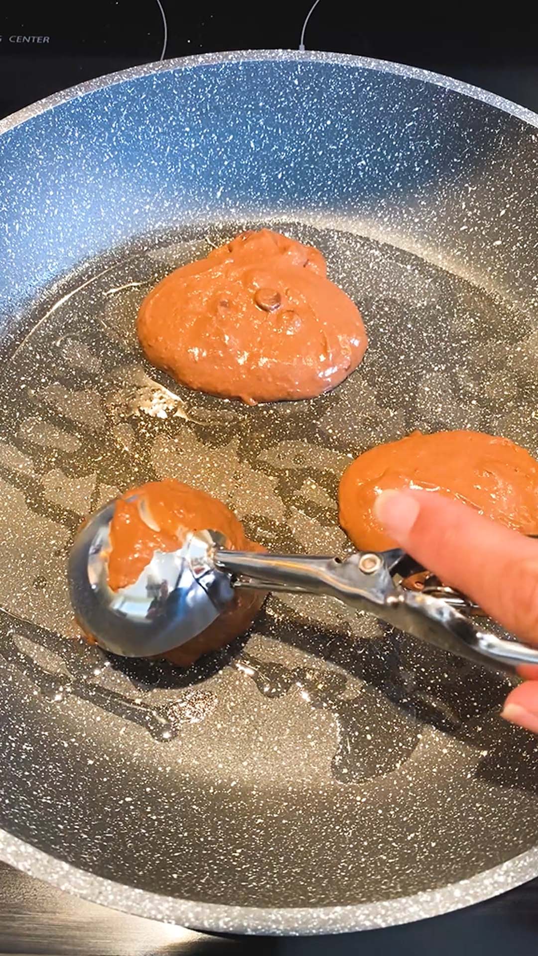 Dropping pancake batter into a skillet with a cookie scoop.