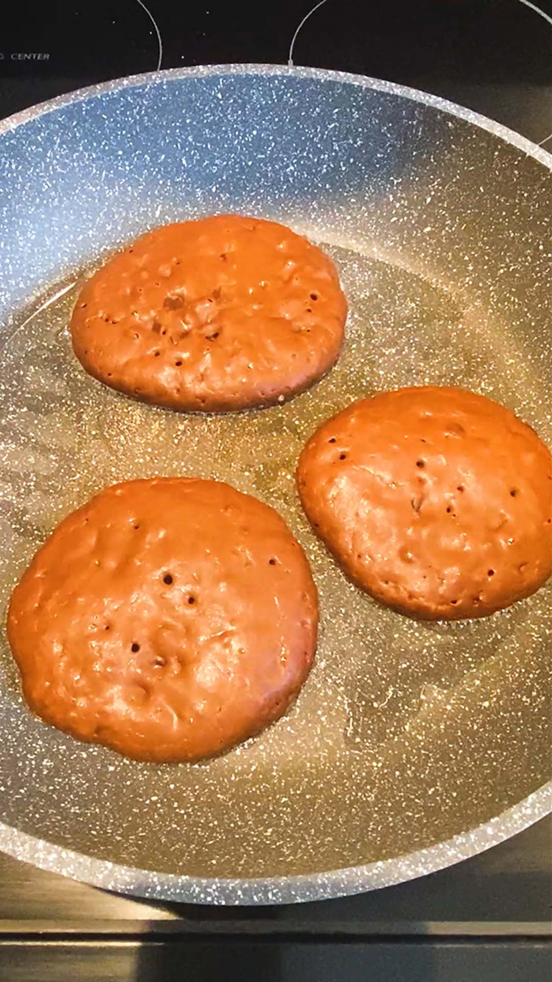 Three pancakes being cooked in a skillet.
