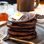 A stack of pancakes with a pat of butter on top and syrup being poured on.