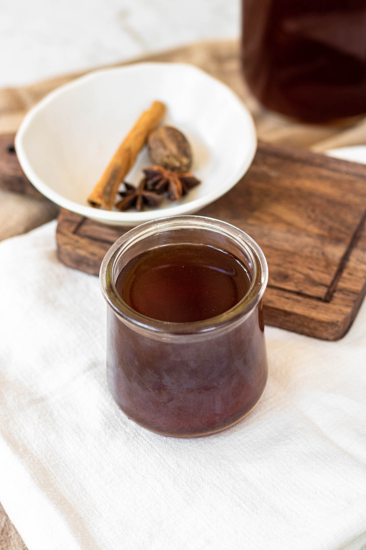A cinnamon stick, nutmeg seed, and anise star in a bowl next to a glass of tea concentrate.