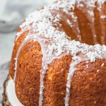 A whole bundt cake with icing and coconut on top.