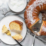 A slice of coconut bundt cake on a plate beside the cake.