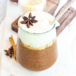 A cup with dark coffee on the bottom and white foamed milk on top, garnished with an anise star..