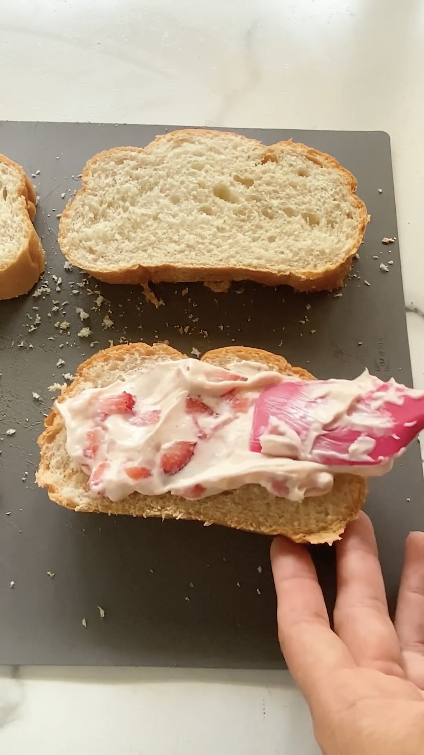 Spreading strawberry cream cheese mixture onto a slice of bread.