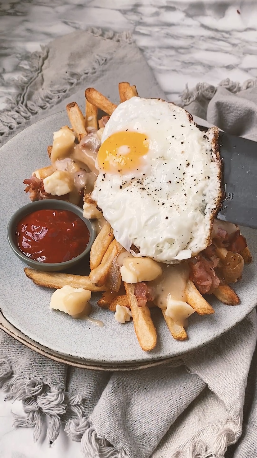 Adding an egg to fries topped with cheese curds, gravy, and bacon..