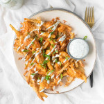 Fries on a plate covered in chicken, buffalo sauce, cheese, and green onions.