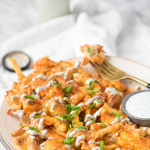 Fries on a plate covered in chicken, buffalo sauce, cheese, and green onions.