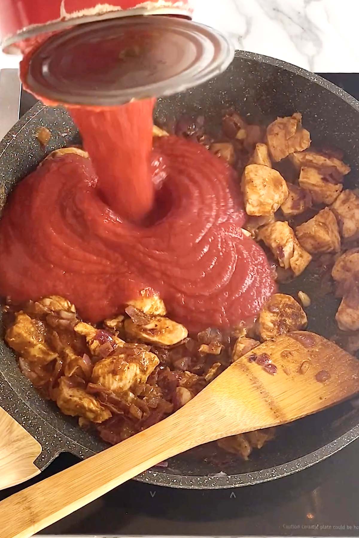 Adding crushed tomatoes to a pan of spiced chicken.