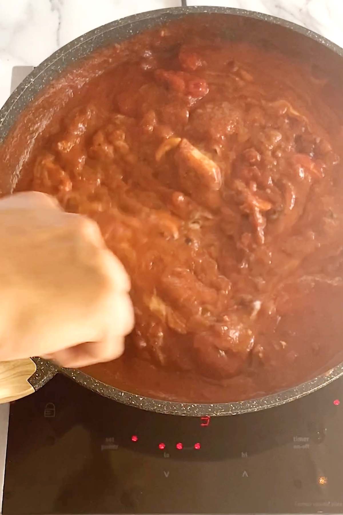 Stirring butter chicken sauce in a pan.