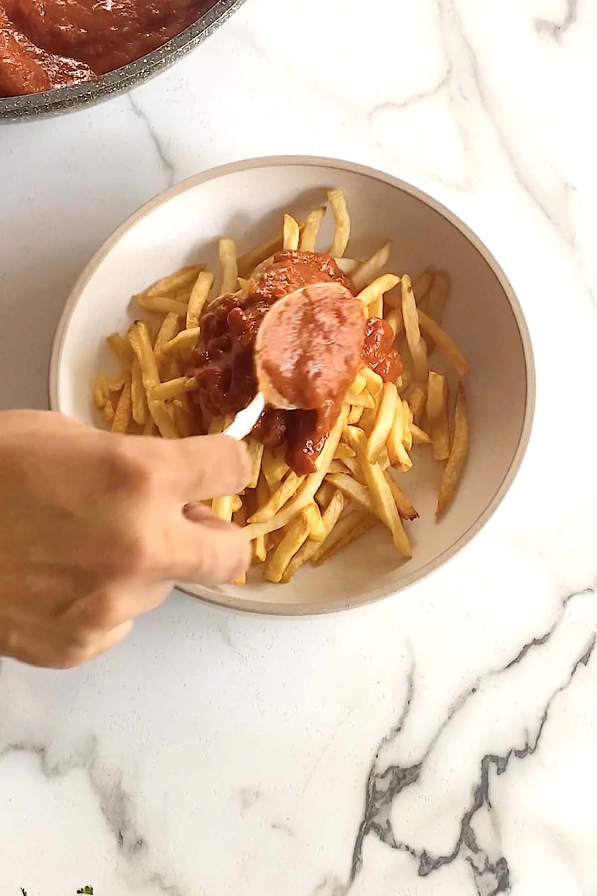 Spooning butter chicken sauce on top of fries.
