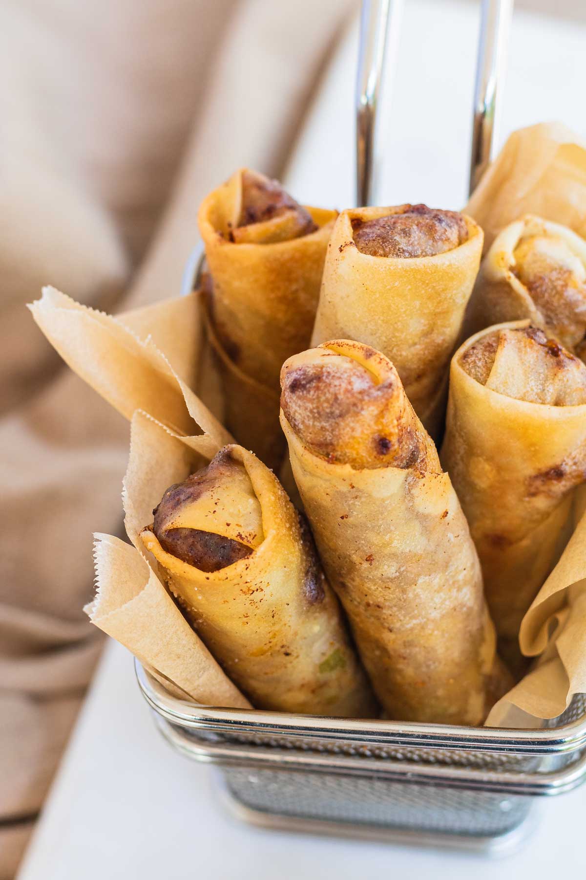 Cheeseburger spring rolls standing on end in metal fry baskets.