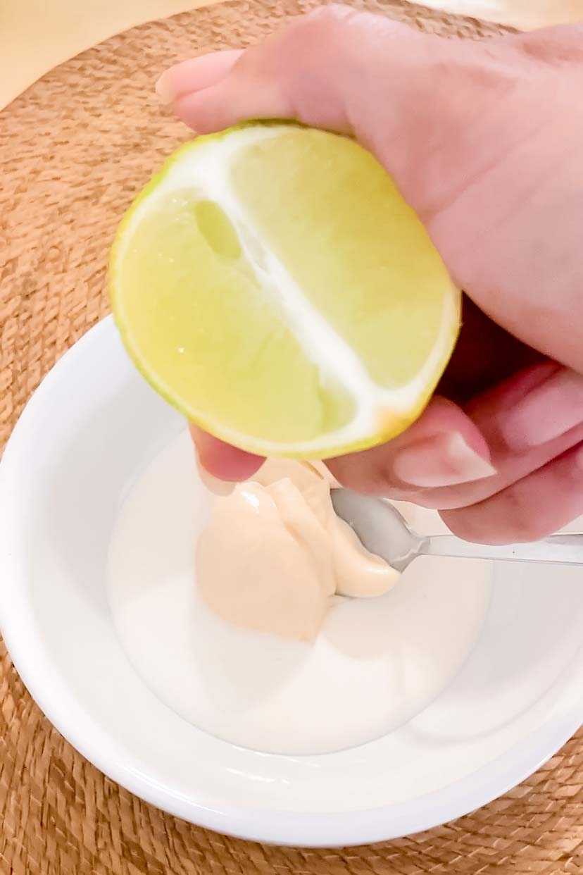 Holding a lime over a bowl or mayo and crema.