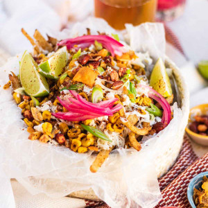 Fries in a basket topped with corn, mayo, peanut, and pickled red onions.