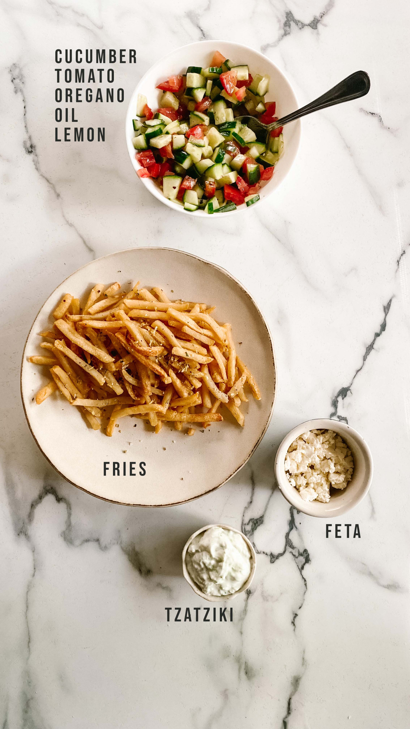 Ingredients for Greek fries on a marble counter with text labels.