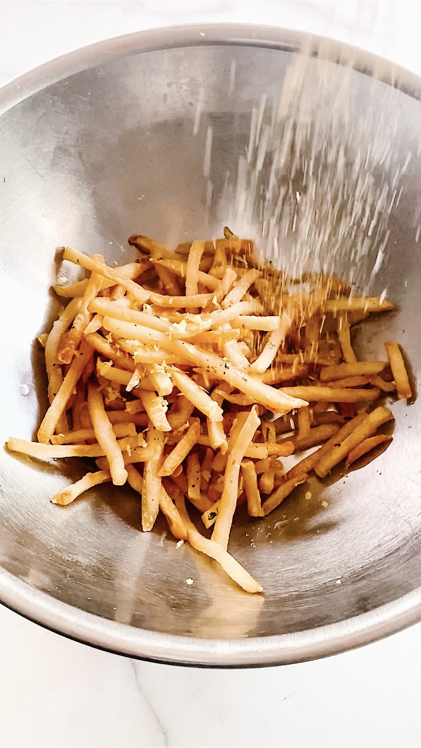 Seasoning fries in a stainless steel bowl.