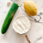 Ingredients for tzatziki sauce on a white marble counter.