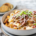 Fries, perogies, cheese curds, bacon, green onions, and drizzled sour cream in a bowl with a text title.