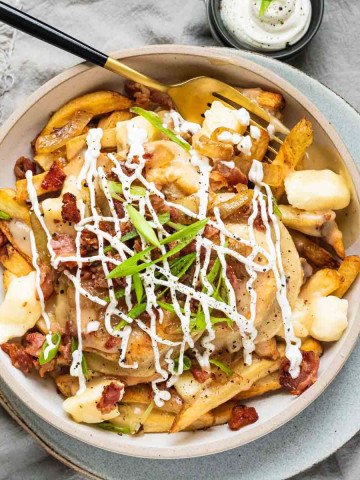 Fries, perogies, cheese curds, bacon, green onions, and drizzled sour cream in a bowl.