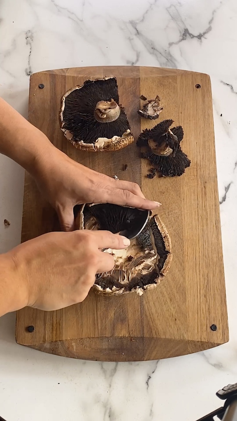 Removing the gills from portobello mushroom caps with a spoon.
