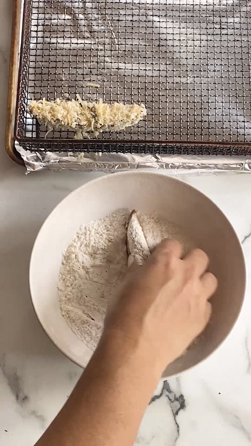 Dipping a portobello slice into flour.