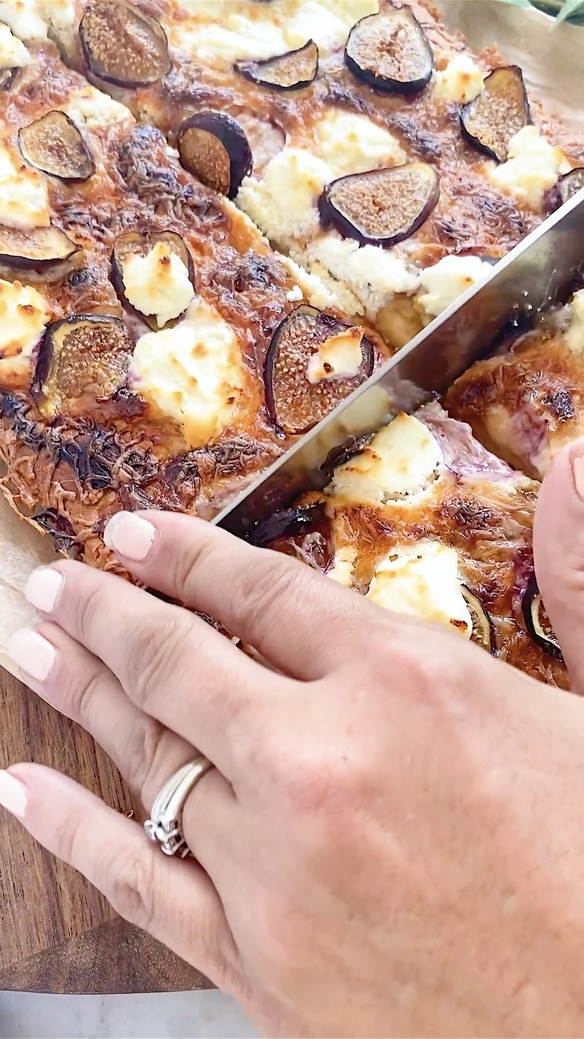 Cutting a pizza with figs and goat cheese.