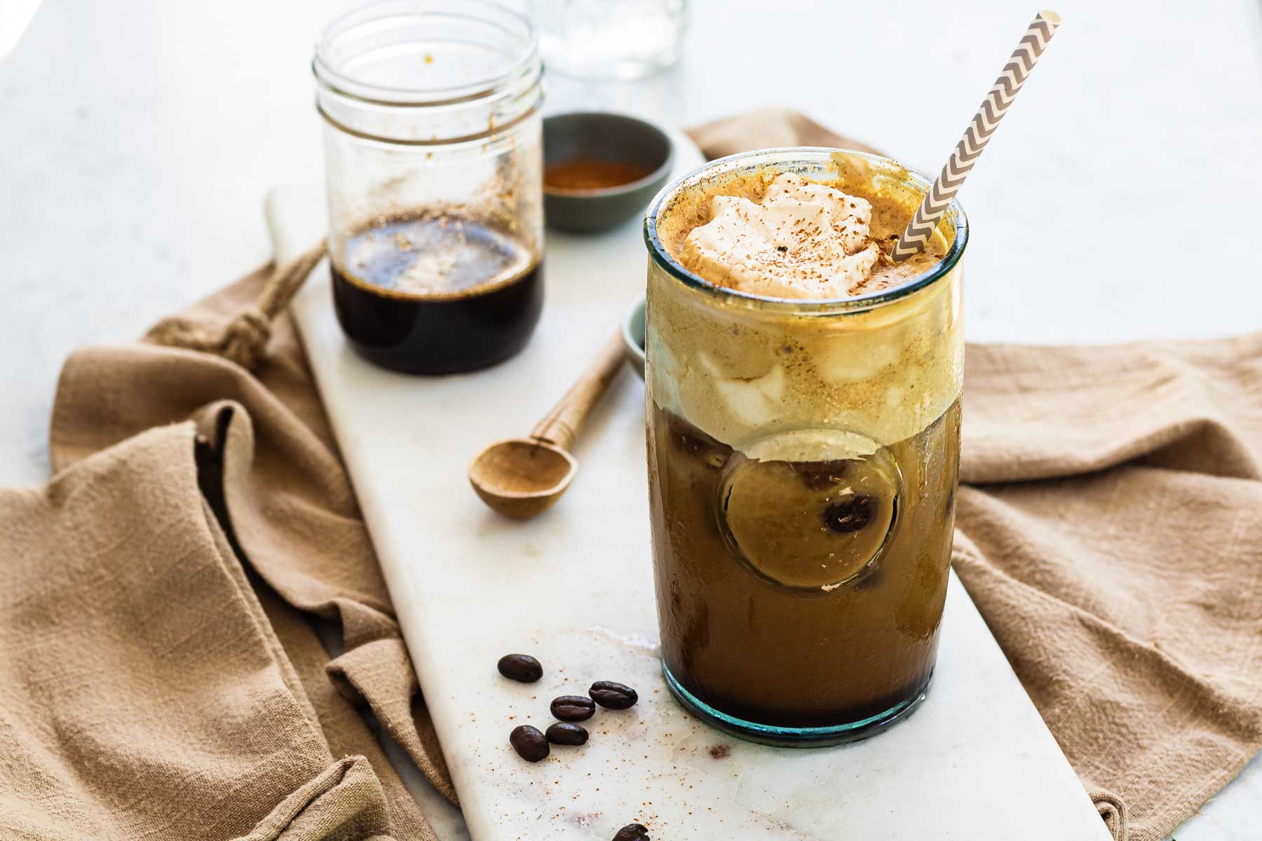 An iced coffee in a glass with whipped topping on top and cinnamon.