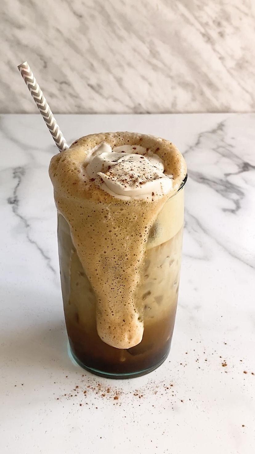 An iced coffee in a glass with whipped topping on top and cinnamon.