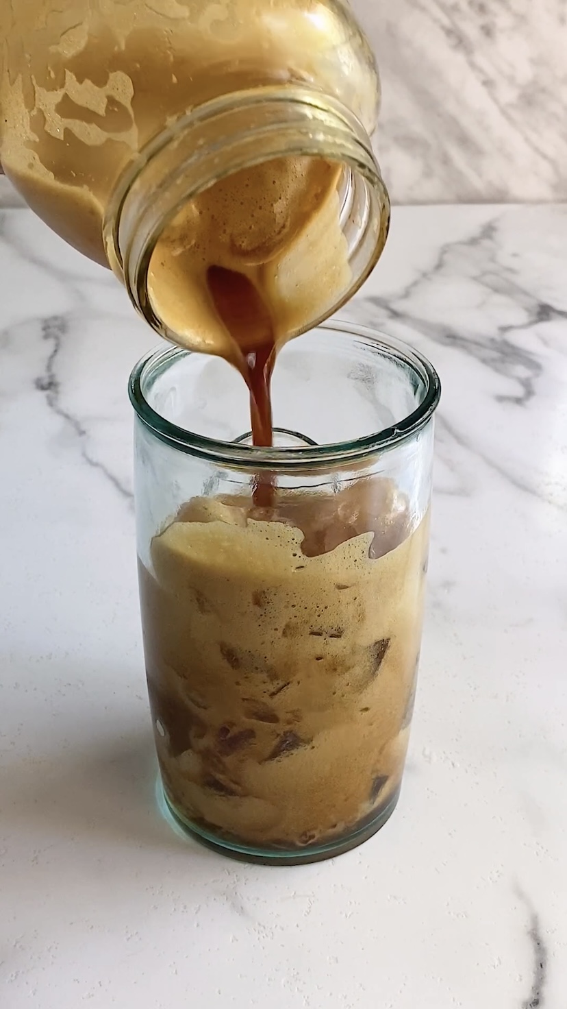Pouring shaken espresso into a glass with ice.