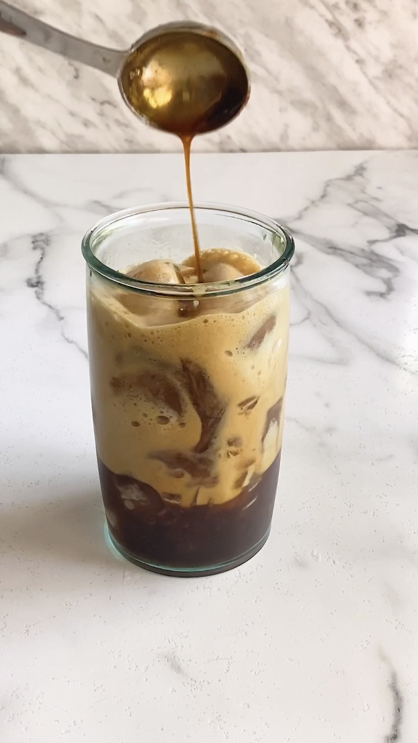 Adding brown sugar syrup to a glass with iced coffee in it.