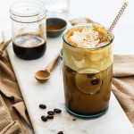 An iced coffee in a glass with whipped topping on top and cinnamon.