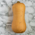 A whole butternut squash on a marble counter.