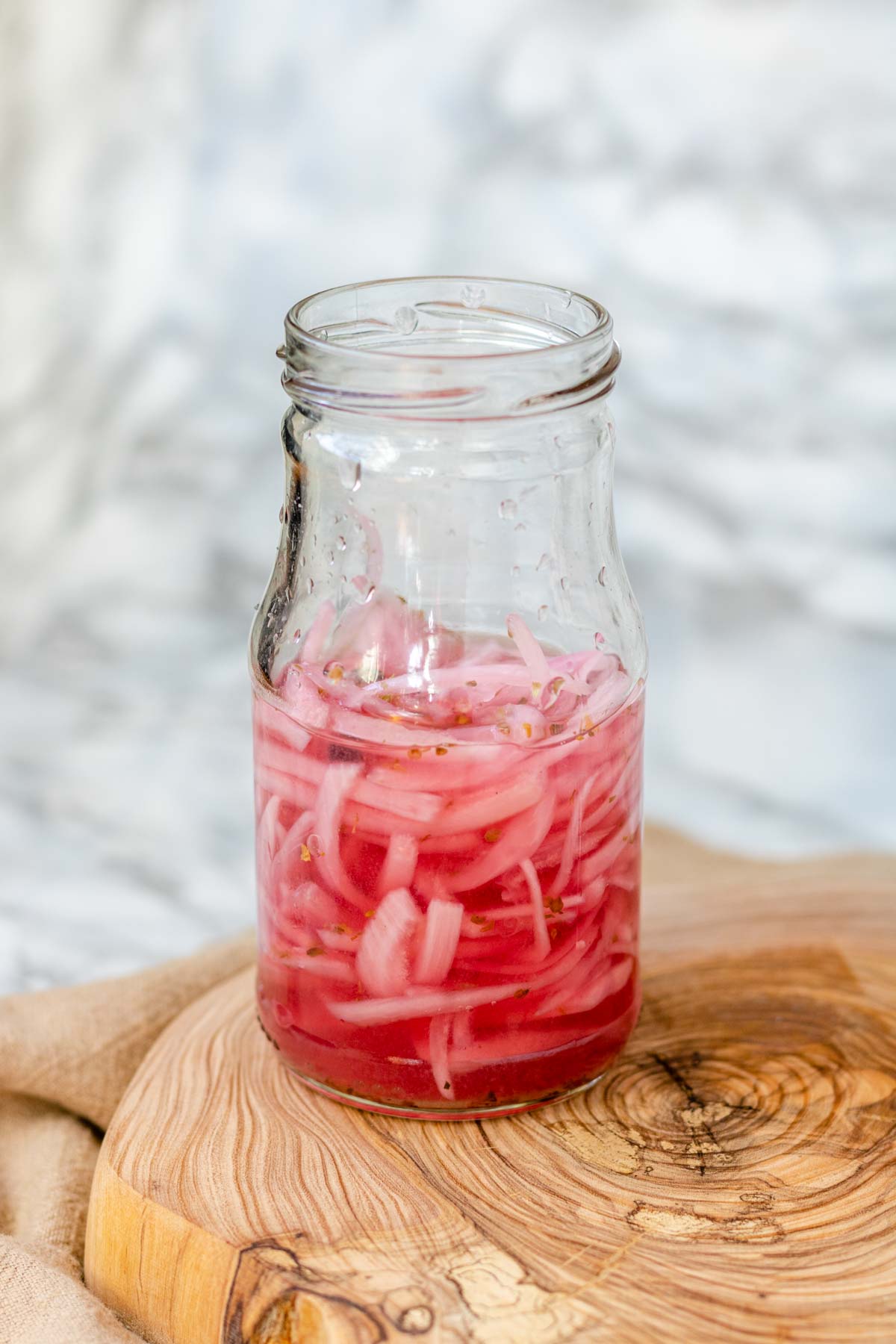 Pink pickled red onions in a clear jar.