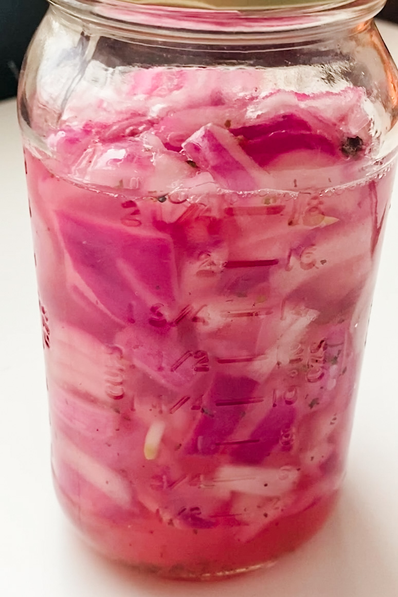 Bright pink pickled onions in a jar of liquid.