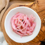 Pink pickled red onions in a white bowl.