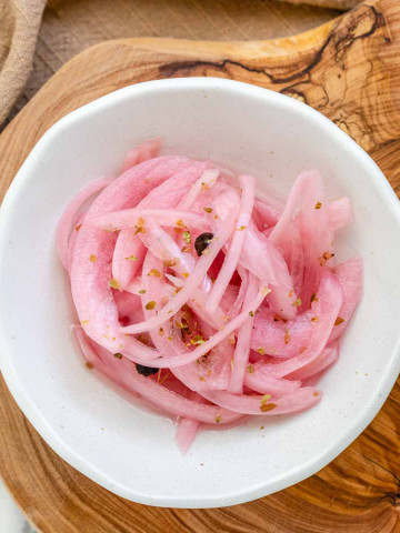 Pink pickled red onions in a white bowl.