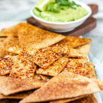 Baked and seasoned tortilla chips on a marble platter with avocado sauce.