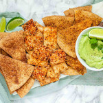 Baked and seasoned tortilla chips on a marble platter with avocado sauce.