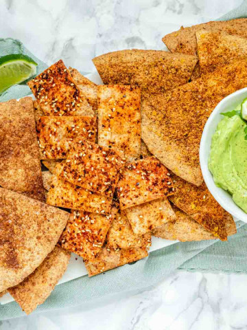 Baked and seasoned tortilla chips on a marble platter with avocado sauce.