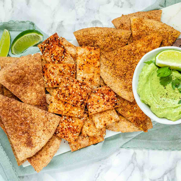Baked and seasoned tortilla chips on a marble platter with avocado sauce.