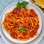 A plate of bucatini noodles with red bolognese sauce on top.