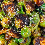 A bowl of roasted Brussels sprouts with sauce and sesame seeds on them.