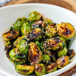 A bowl of roasted Brussels sprouts with sauce and sesame seeds on them.