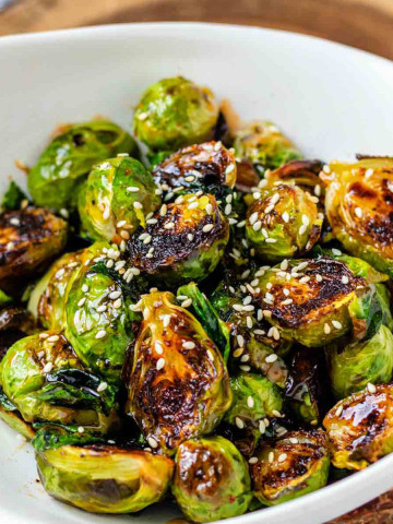 A bowl of roasted Brussels sprouts with sauce and sesame seeds on them.